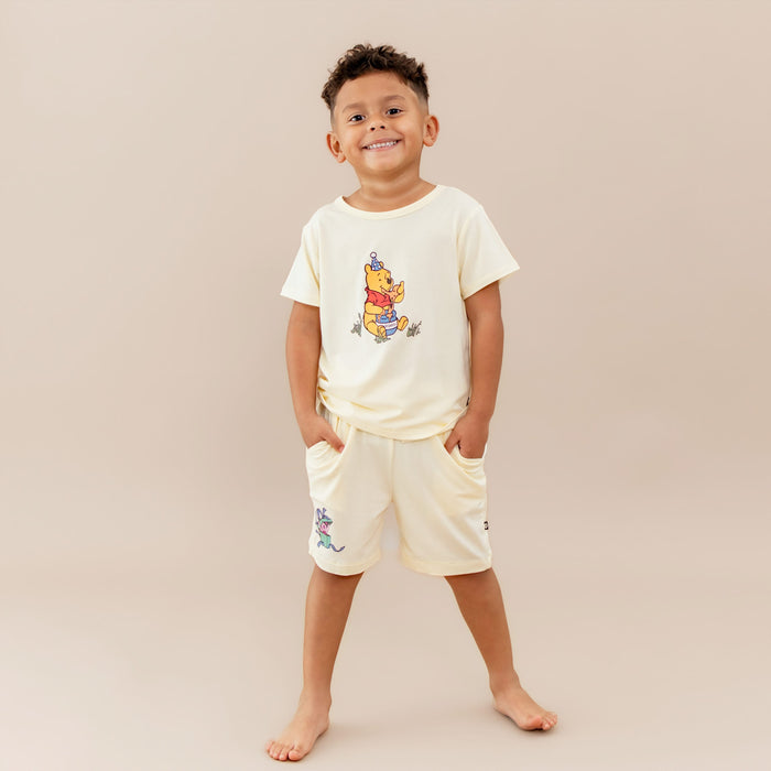 Young smiling boy wearing the Toddler Basic Tee in Winnie the Pooh on Chamomile paired with the Winnie the Pooh drawstring shorts on chamomile