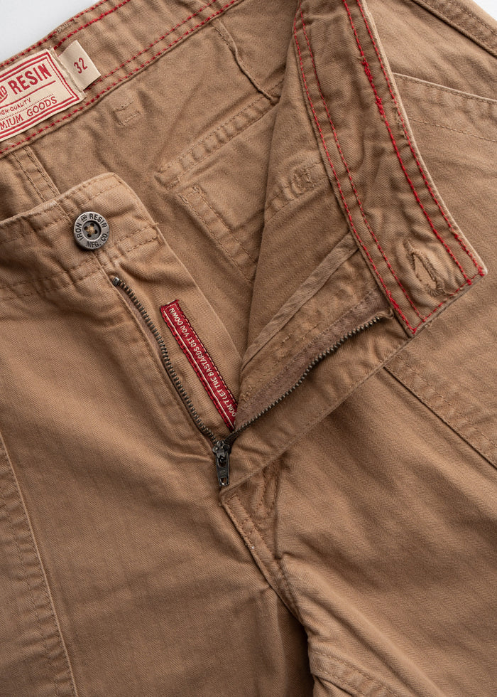 Close-up of khaki pants with red stitching, open zipper, and visible label. Size 32. Premium goods tag on waistband.