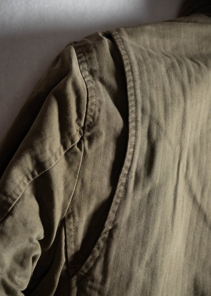 Close-up of a khaki jacket shoulder, highlighting the fabric texture and stitching details in soft light.