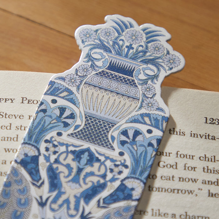 A close-up of the Liberty Oscars Palace Shaped Bookmark by Liberty of London Ltd, featuring a blue and white ornate vase and floral design inspired by the iconic Liberty Oscars Palace print, resting on an open book against a wooden background.