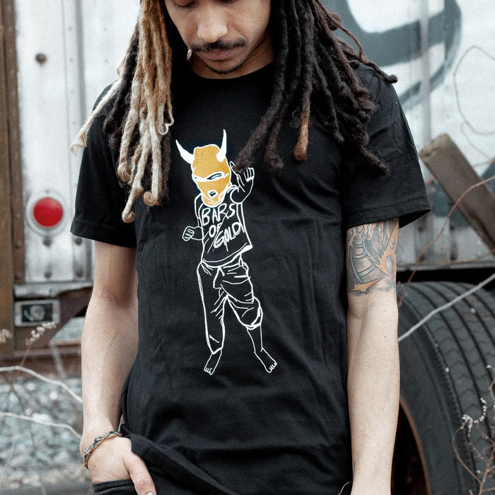 Black short sleeve shirt with a person outlined in white. The person is wearing a red mask with devil horns and a shirt that says BARS OF GOLD on it. An individual is modeling the shirt and standing outside next to a truck.
