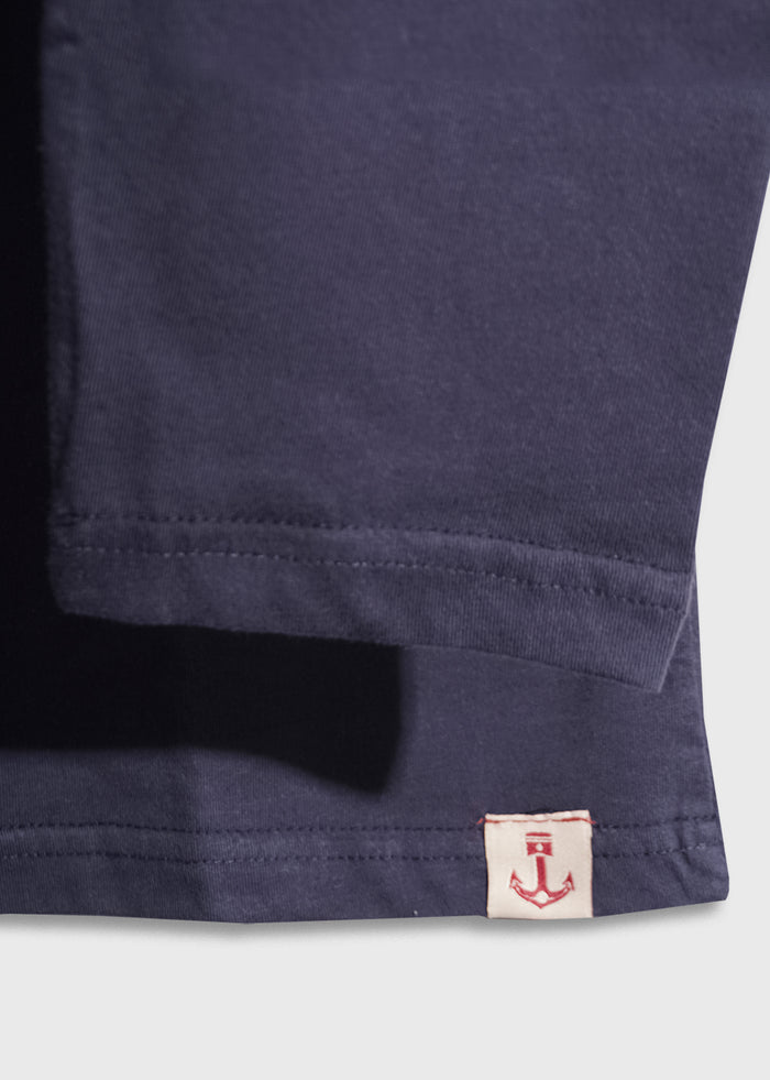 Close-up of a navy shirt's hem with a small white tag featuring a red anchor design, highlighting the garment's nautical theme.