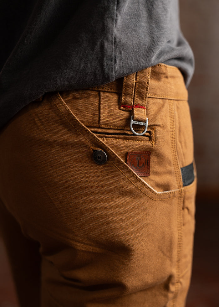 Close-up of brown pants with a buttoned pocket and a metal loop, paired with a dark shirt, emphasizing casual style.