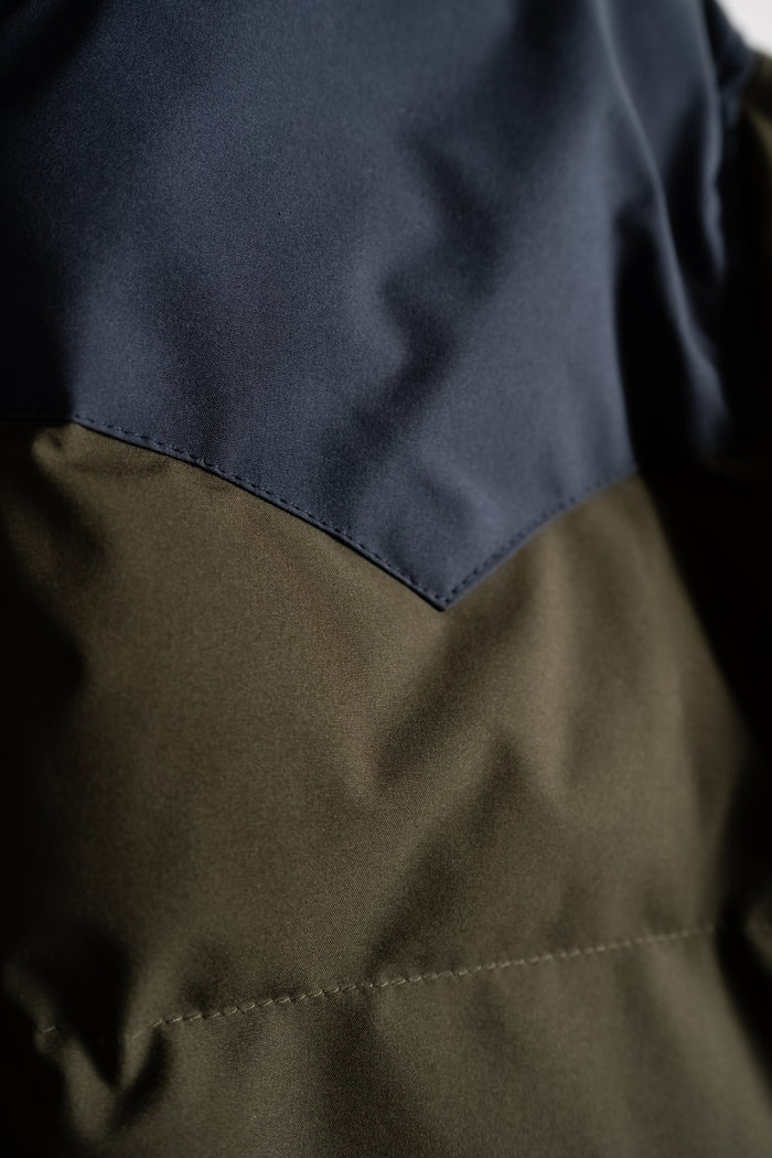 Close-up of a jacket with navy and olive fabric, showing a sharp seam detail.
