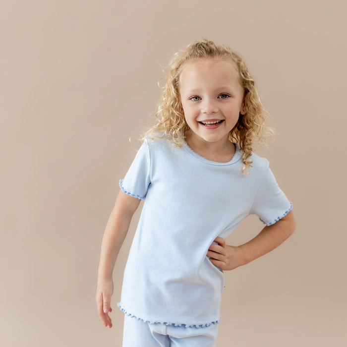 Young girl wearing a light blue pointelle lounge set against a beige background