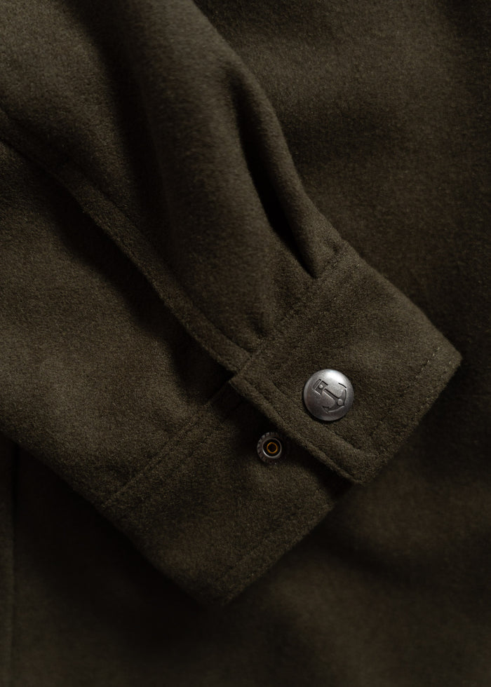 Close-up of a dark green wool coat sleeve with a silver button and detailed stitching, highlighting its texture and design.