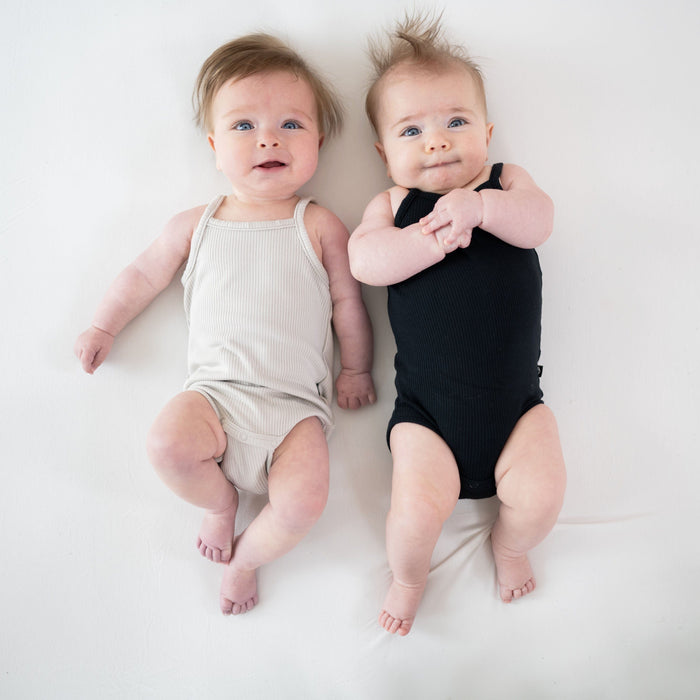 Babies wearing Kyte Baby Ribbed Spaghetti Strap Bodysuits in Oat and Midnight