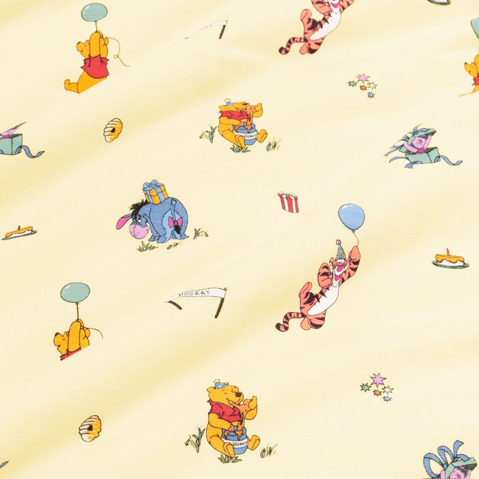 Close up of fabric swatch of the Winnie the Pooh Celebration print showing the story book characters on a yellow background