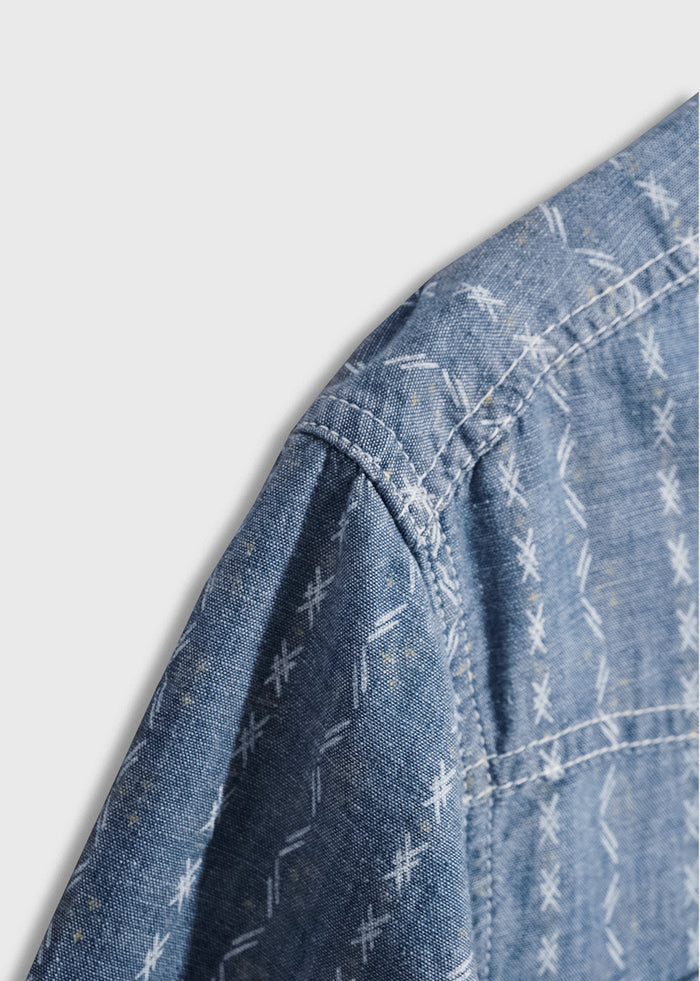 Close-up of a blue denim shirt with white geometric patterns, showcasing detailed stitching on the shoulder area.