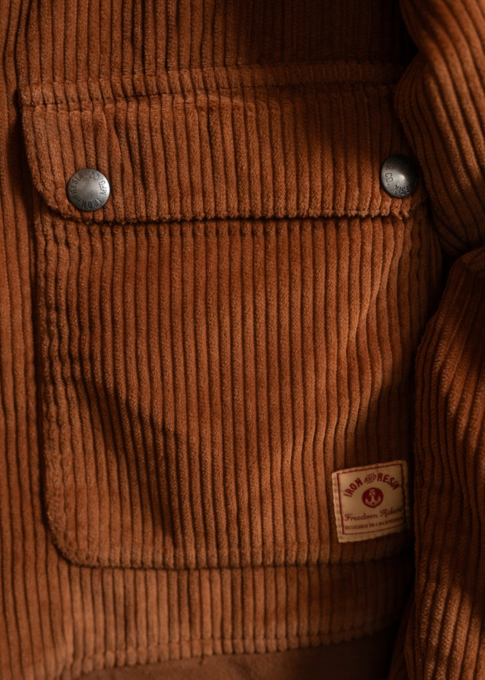 Close-up of a brown corduroy jacket pocket with metal buttons and a label reading "Iron and Resin, Freedom Riders."
