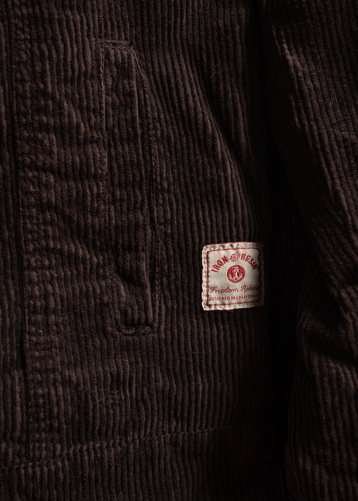 Close-up of a brown corduroy jacket with a visible pocket and an "Iron and Resin" label, highlighting texture and brand detail.
