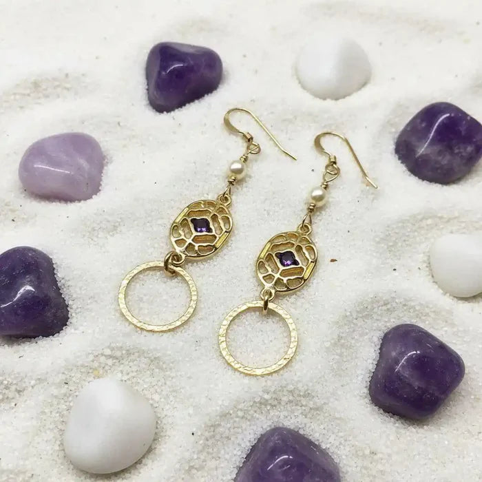 14 K Gold Filled Purple Crystal Circle Filigree Earrings with pearls on a sandy surface.