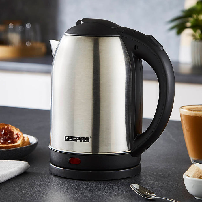 The image shows off the geepas stainless steel kettle on top of a kitchen countertop with a cup of coffee and a piece of toast with jam besides it.