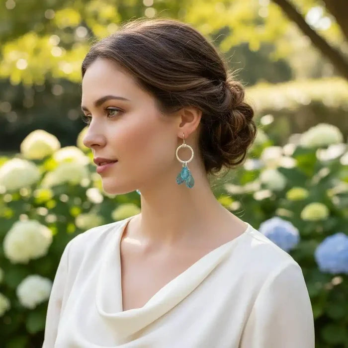 A model wearing 925 Silver Hammered Aqua Crystal Cascading Drop Earrings in a garden setting.