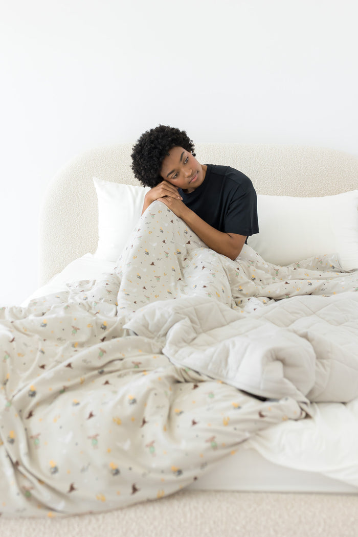 Person lying in bed under a soft, Harry Potter patterned adult blanket in a minimalistic room.