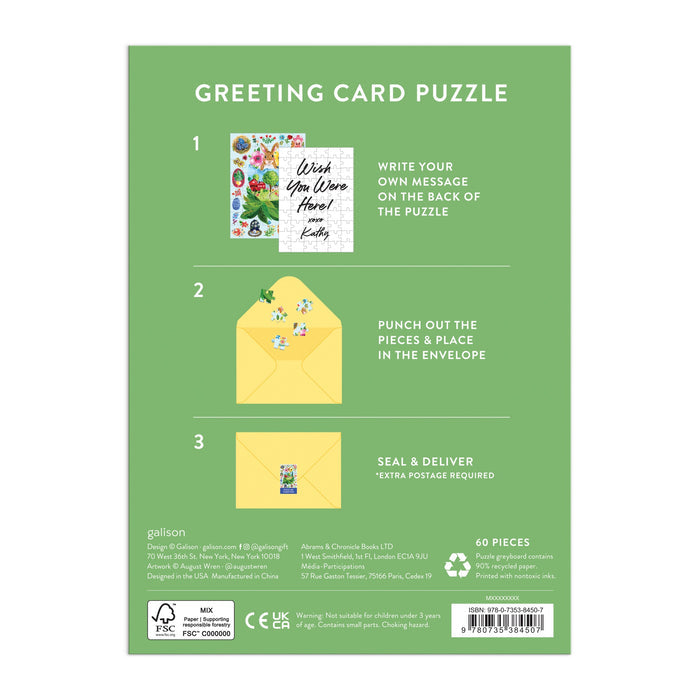 Back of a green Artisanal Eggs Greeting Card Puzzle box (Jennifer O Lewis/August Wren) shows steps: 1. Write wishes on puzzle back, 2. Punch out pieces and place in yellow envelope, 3. Seal and deliver. Includes images of card, puzzle pieces, and envelopes.