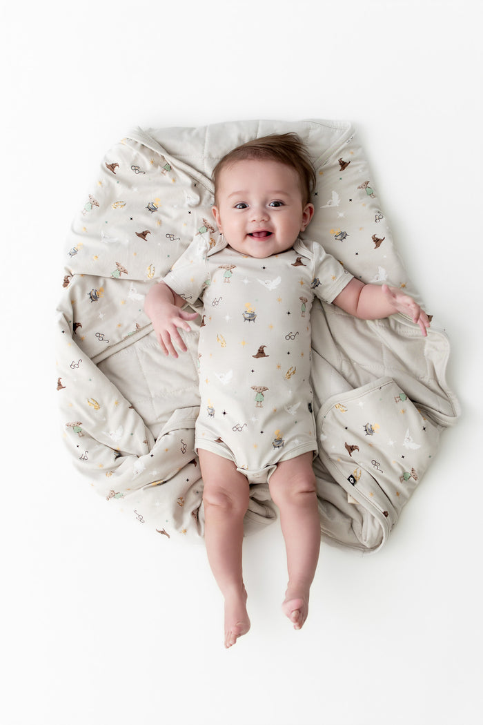 Baby wrapped in a beige baby blanket with Harry Potter patterns wearing a similar bodysuit on a white background