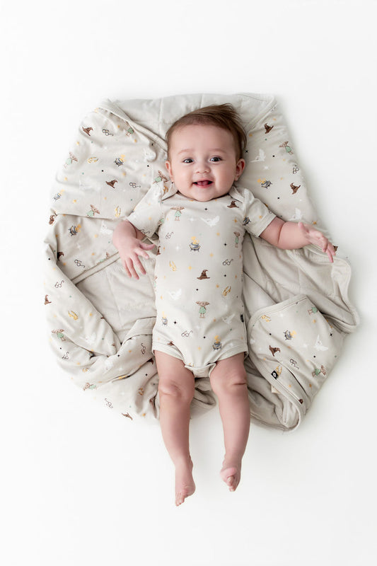Baby wrapped in a beige baby blanket with Harry Potter patterns wearing a similar bodysuit on a white background