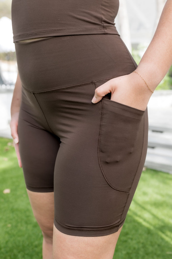 Female model wearing the Bamboo Flex High Rise Biker Short in Espresso with one hand in the side pocket