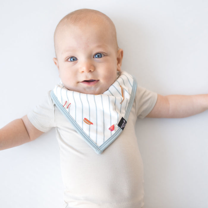 Young baby wearing the Bib in Home Run overtop a light cream short sleeve bodysuit