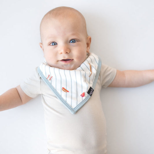 Young baby wearing the Bib in Home Run overtop a light cream short sleeve bodysuit