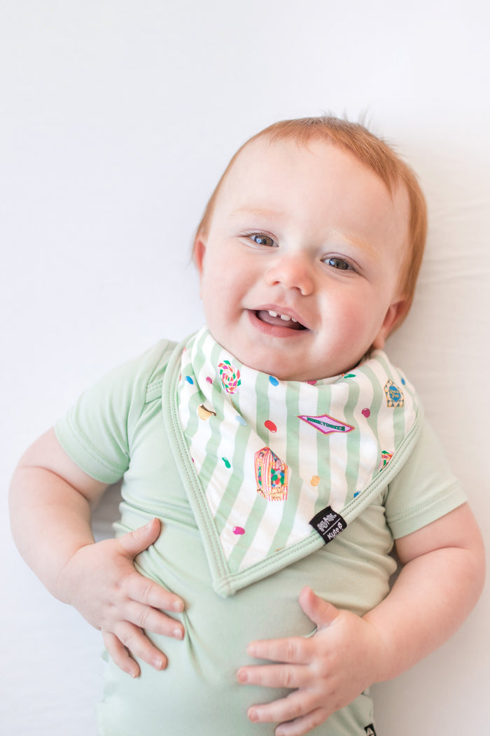 Baby wearing a green and white striped bib with colorful Harry Potter patterns and a green bodysuit on a white background