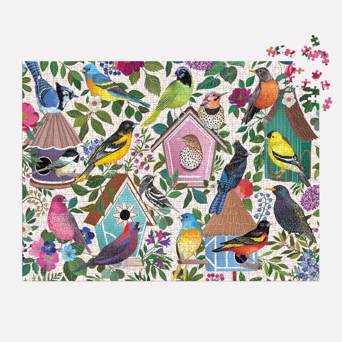 The Birdhouse Lane 1000 Piece Puzzle by Christine De Carvalho features vibrant birds and ornate birdhouses among lush leaves and flowers, with several pieces missing from the top right corner.