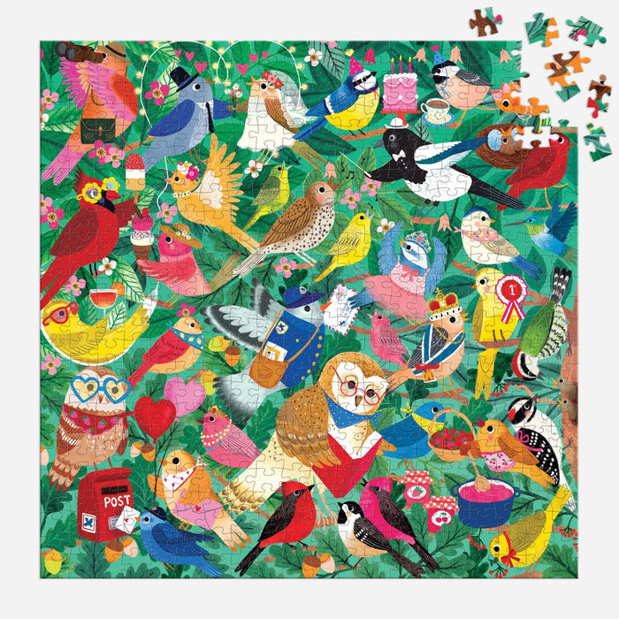 The Birding Around 500 Piece Puzzle by Rebecca Jones features illustrated birds with accessories among green leaves; some pieces are missing from the top right, with loose pieces nearby.