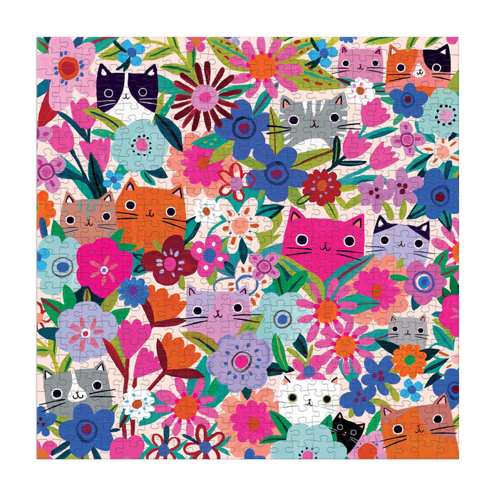 The Tara Lilly Blooming Cats 500 Piece Puzzle features playful orange, gray, pink, and black cats with wide eyes peeking from lush flowers and green leaves for a colorful, delightful challenge.