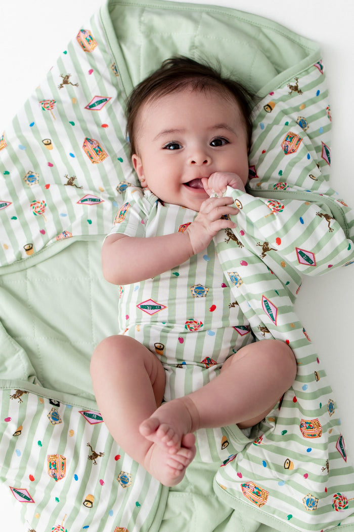Baby wrapped in a green and white stripped baby blanket with cartoon Harry Potter patterns, wearing a bodysuit with the similar print.