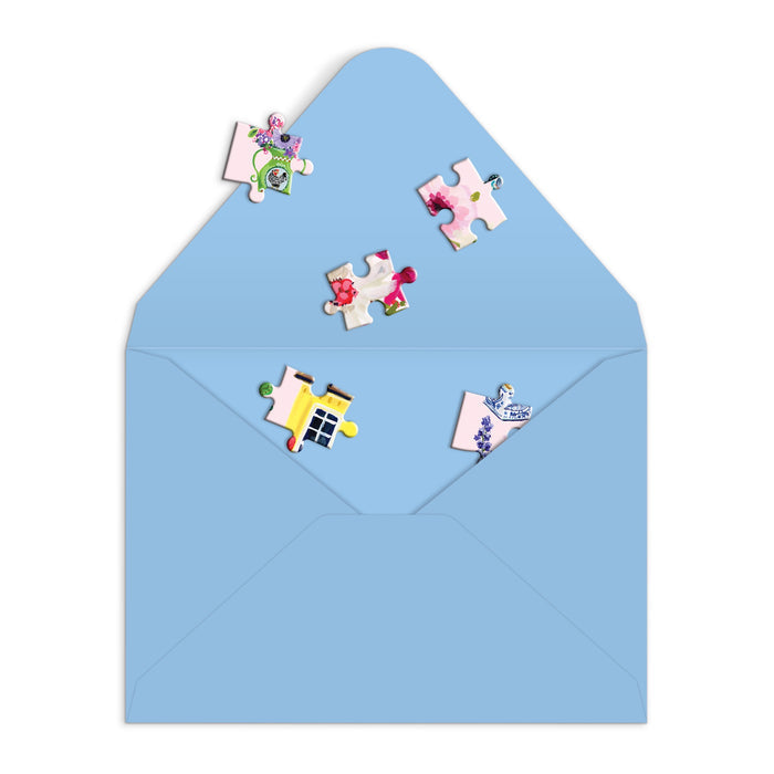 A playful Buzzy Bouquets Greeting Card Puzzle by Jennifer O Lewis/August Wren features a blue envelope with colorful jigsaw pieces spilling out onto a white background—perfect for any occasion.