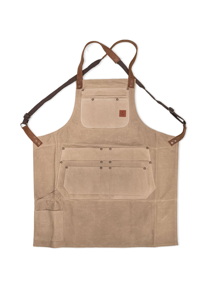 Tan canvas apron with brown leather straps and multiple pockets, designed for utility and style in cooking or crafting tasks.