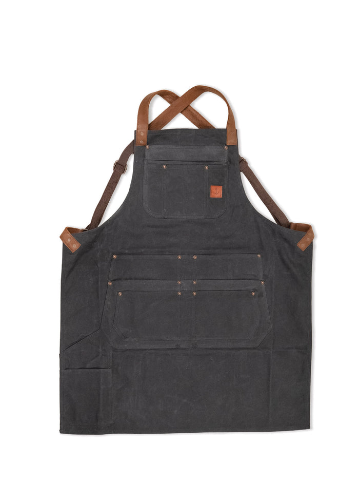 Dark canvas apron with brown leather straps and multiple pockets, designed for durability and functionality in work settings.