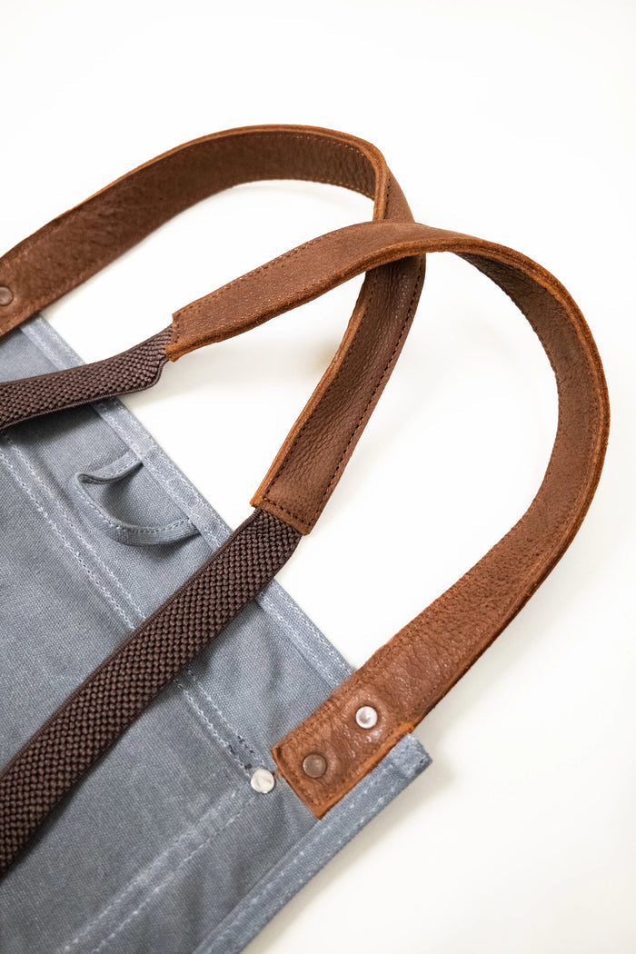 Gray canvas tote bag with brown leather handles and metal rivets, showcasing durable and stylish craftsmanship.