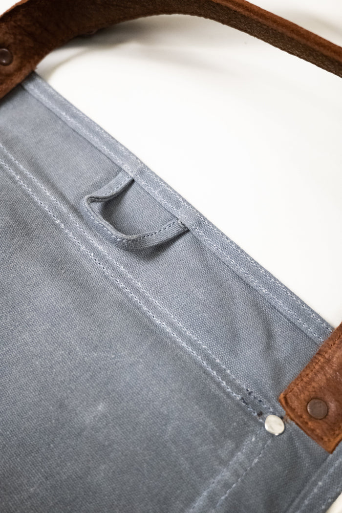 Close-up of a blue canvas bag with brown leather straps and a metal rivet, showcasing durable stitching and texture.