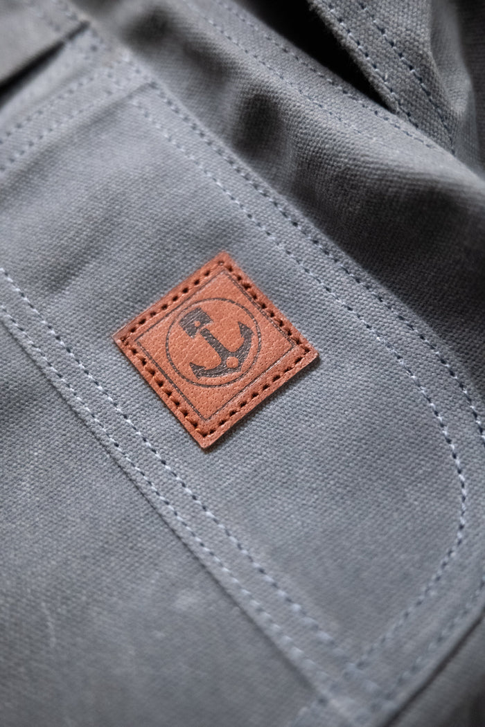 Close-up of a gray fabric with a brown leather patch featuring an anchor symbol, highlighting the texture and stitching details.