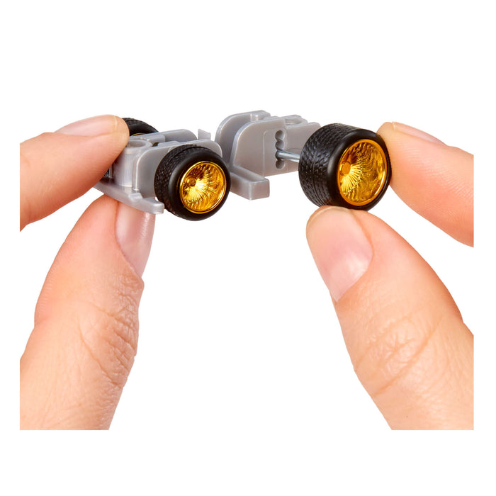 Close-up of hands holding a small car bottom component with gold and black wheels on a white background