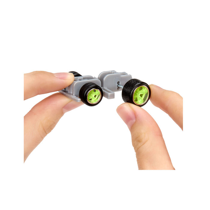 Close-up of hands holding a small car bottom component with green rims and black wheels on a white background