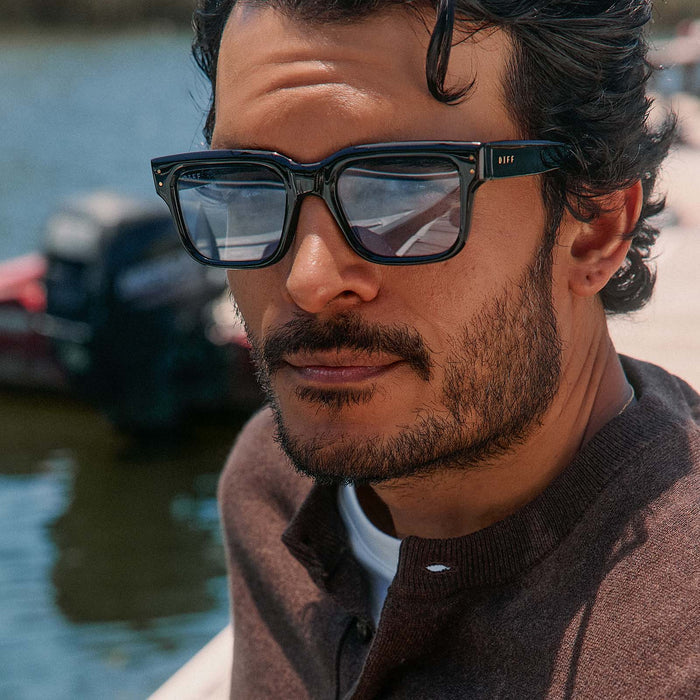 lifestyle - male on a boat dock wearing diff eyewear cash  sunglasses with a black acetate frame and light blue tint lenses front view
