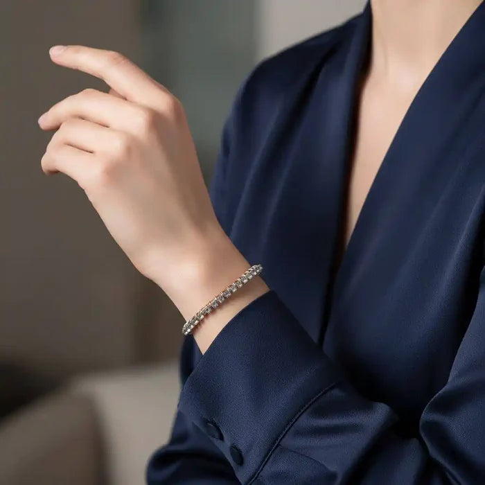 A close-up of a hand wearing a Catch-Free Crystal Rhinestone Tennis Bracelet Bangle on a navy satin blouse.