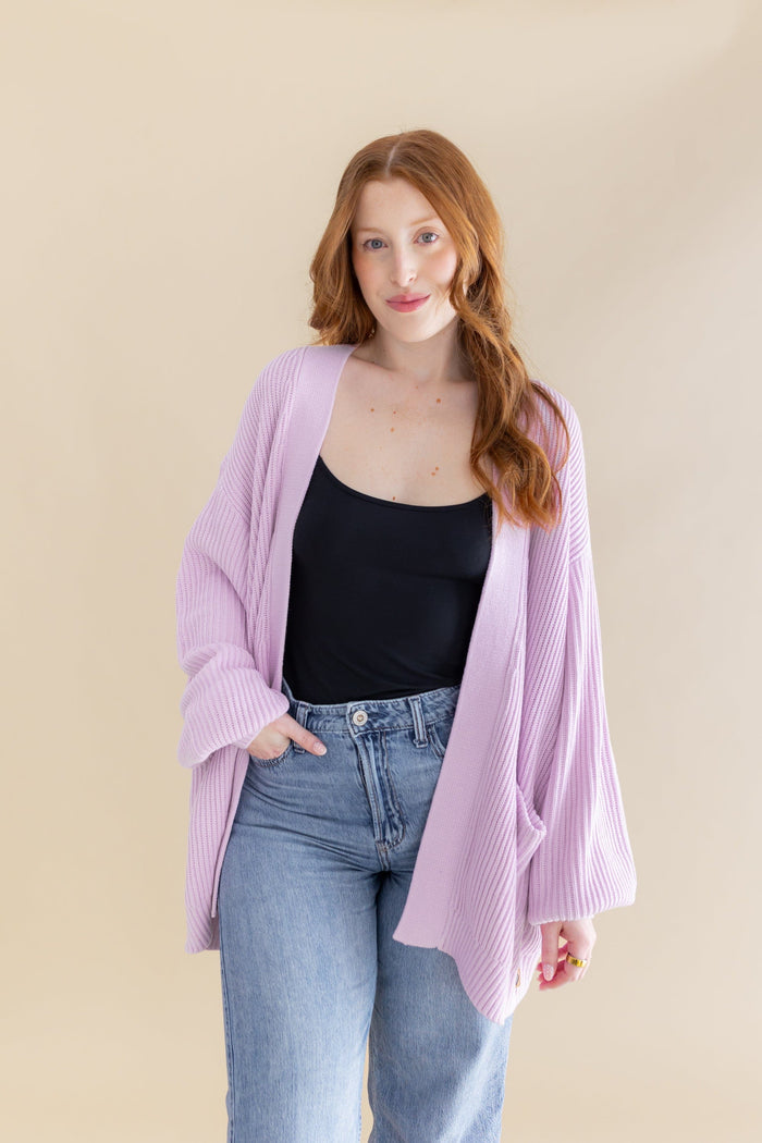 Female posing wearing the Chunky Knit Women's Oversized Cardigan in Thistle with a black camisole and light wash jeans
