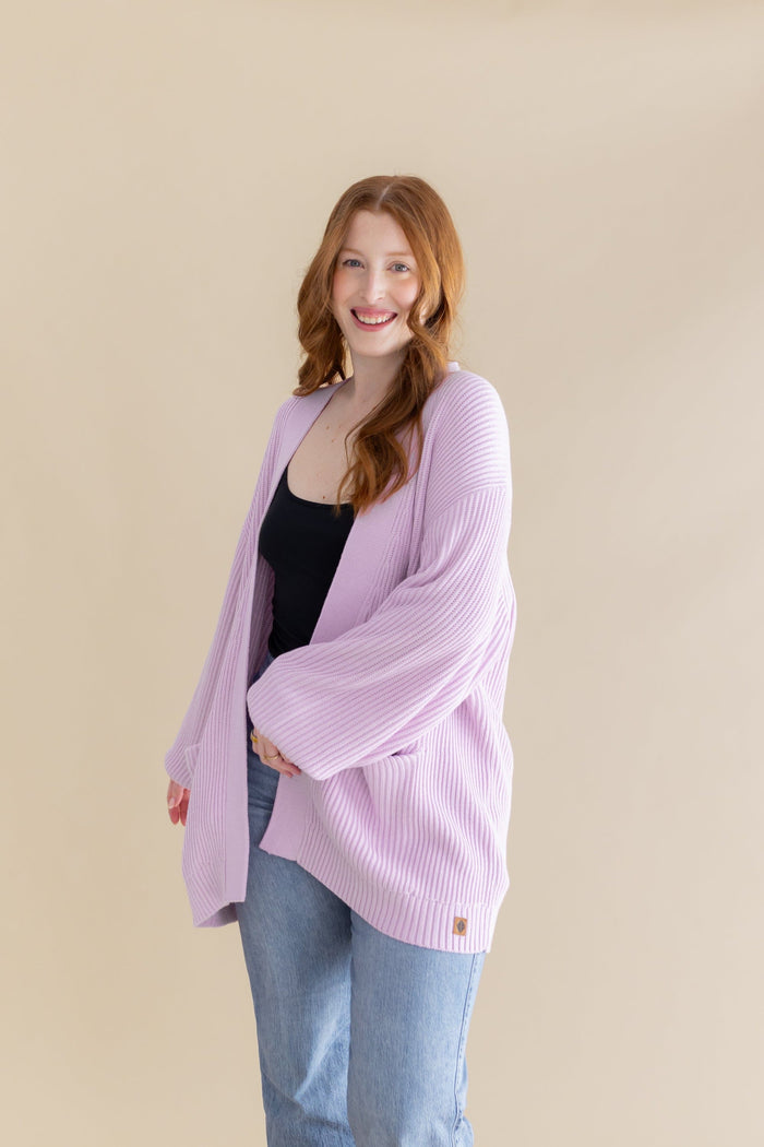 Model posing wearing the Chunky Knit Women's Oversized Cardigan in Thistle paired with a black camisole and light wash jeans