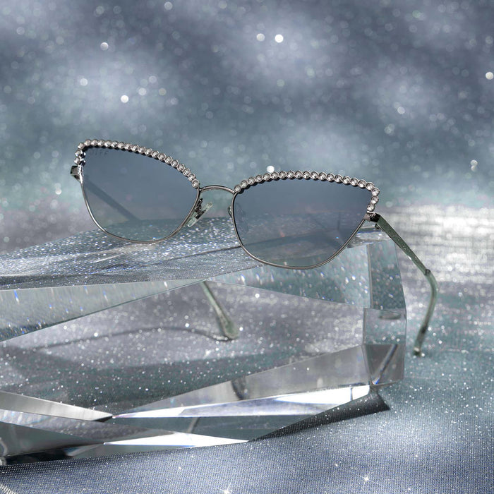 still life - diff eyewear x disney princess featuring the cinderella 2.0 cateye sunglasses with a silver metal frame and grey gradient silver flash lenses front view laying on a piece of glass