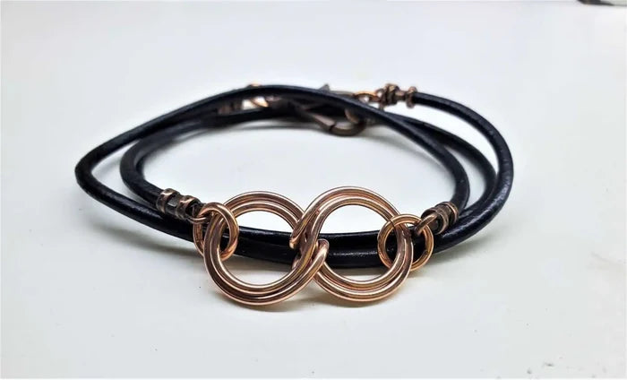 Copper Double Infinity Gender Neutral Leather Wrap Bracelet on a white background with black leather cord and intertwined copper symbols.