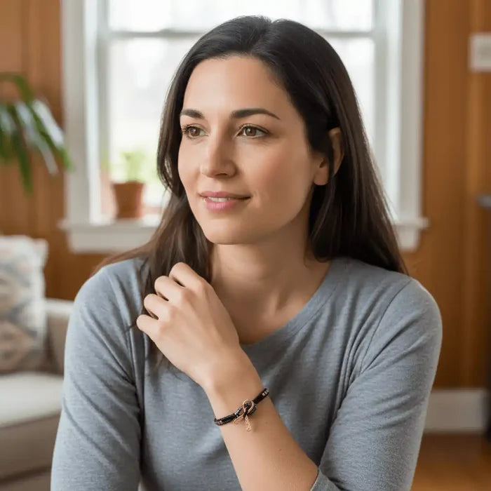 Woman wearing a Copper Ribbon Black Pink Braided Breast Cancer Bracelet in a cozy indoor setting.