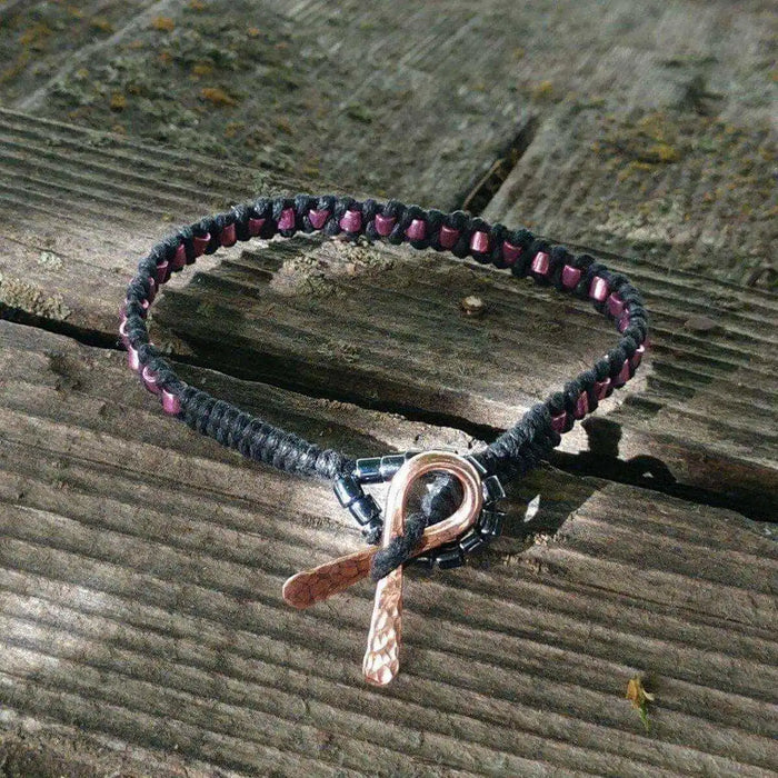 Copper Ribbon Black Pink Braided Breast Cancer Bracelet on a wooden surface showcasing its unique design and features.