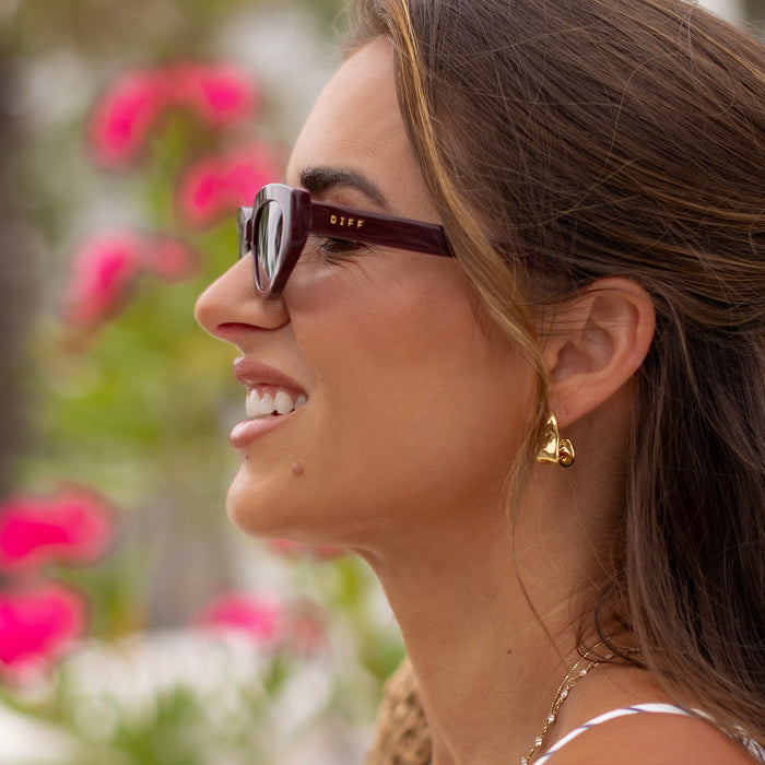 lifestyle - female wearing diff eyewear x jessie james decker crystal cat eye sunglasses with a burgundy red acetate frame and grey gradient polarized lenses side view