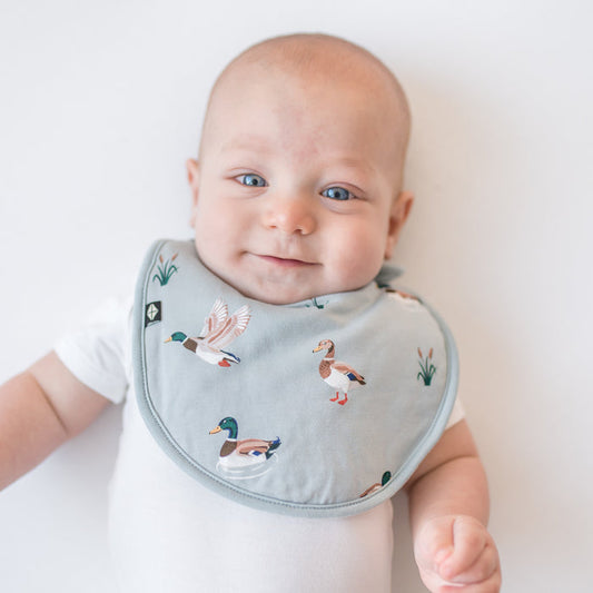 Close up of an infant wearing the Cushy Bib in Mallard Duck paired with a white short sleeve bodysuit