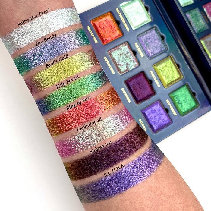 Arm swatches on fair skin tone of all eight eyeshadows included in the Deep Sea Treasures Palette with the palette opened beside arm.