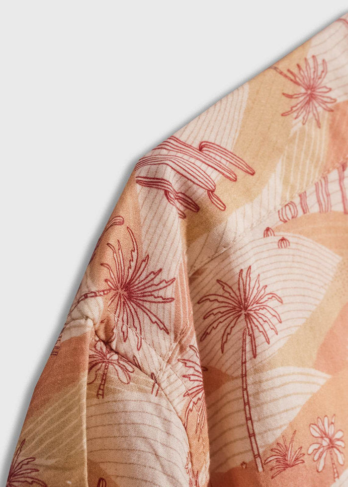 Close-up of a shirt with a tropical palm tree pattern in red and beige tones, showcasing intricate fabric design details.
